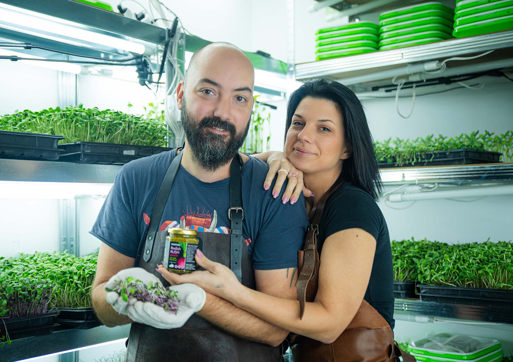 Milena and Ivan Jovanović in their urban farm, holding Moćno products: freshly cut microgreens and microgreens pesto.