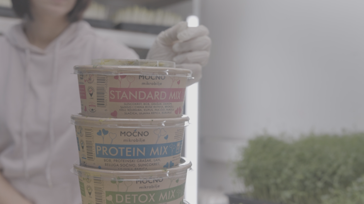Milena Jovanovic holding a stack of microgreens protein mix with visible text on labels.