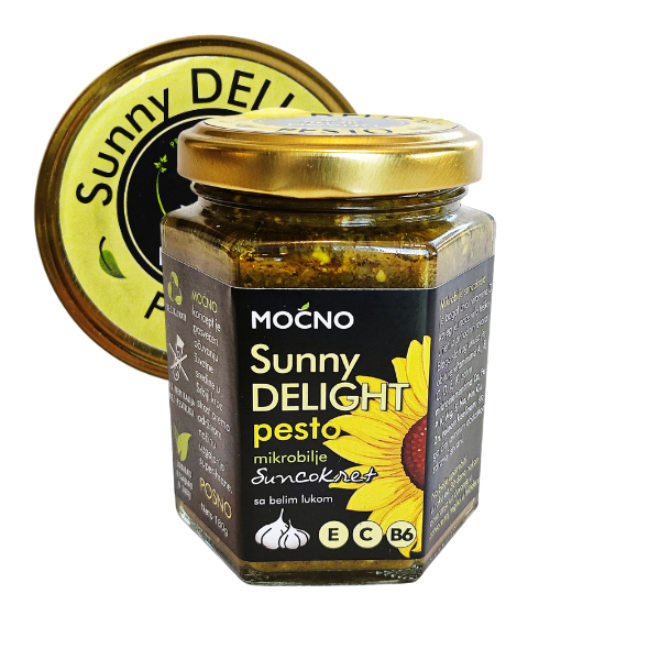 Centralni prikaz šestougaone staklene tegle Sunny Delight pesto namaza. Jasno vidljiva crna etiketa sa ilustracijom suncokreta i zlatni poklopac sa žutom "Sunny Delight" nalepnicom.