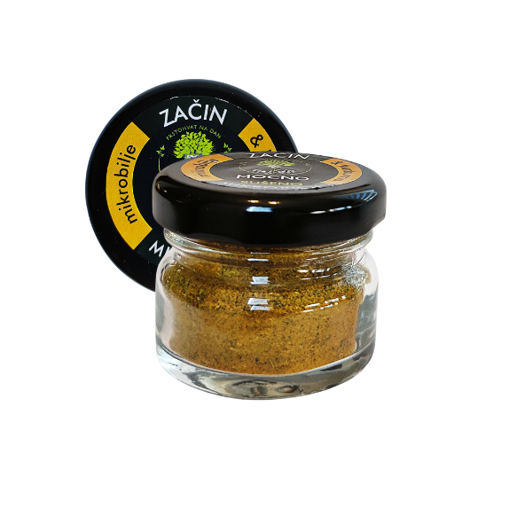 Central view of a small glass jar of MOĆNO dried spice with turmeric. Clearly visible black label with bright yellow details and golden spice powder inside the clear glass.